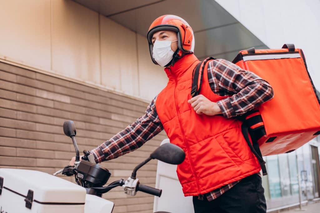 food delivery boy driving scooter with box with food wearing mask